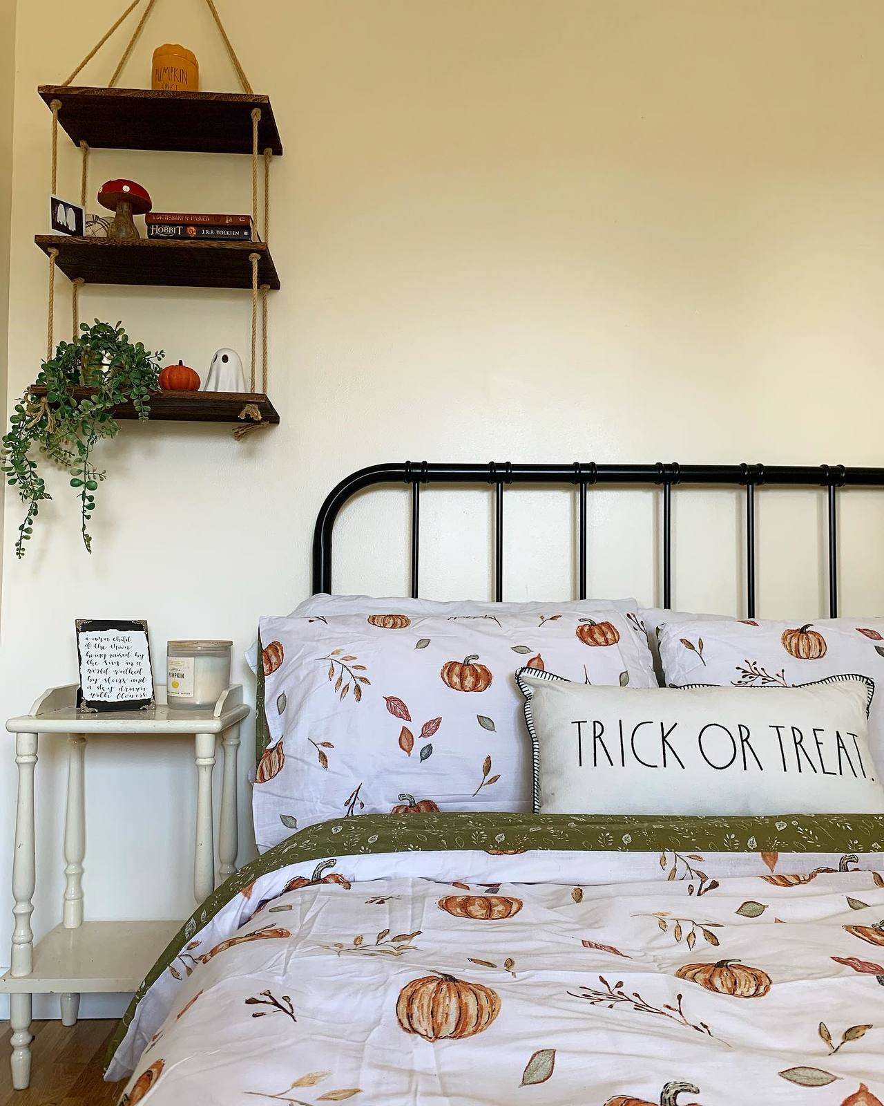 A bright and autumnal room, with pumpkin bedsheets, a boho bedside table, and a hanging shelf with books, plants, and some spooky ghosts.